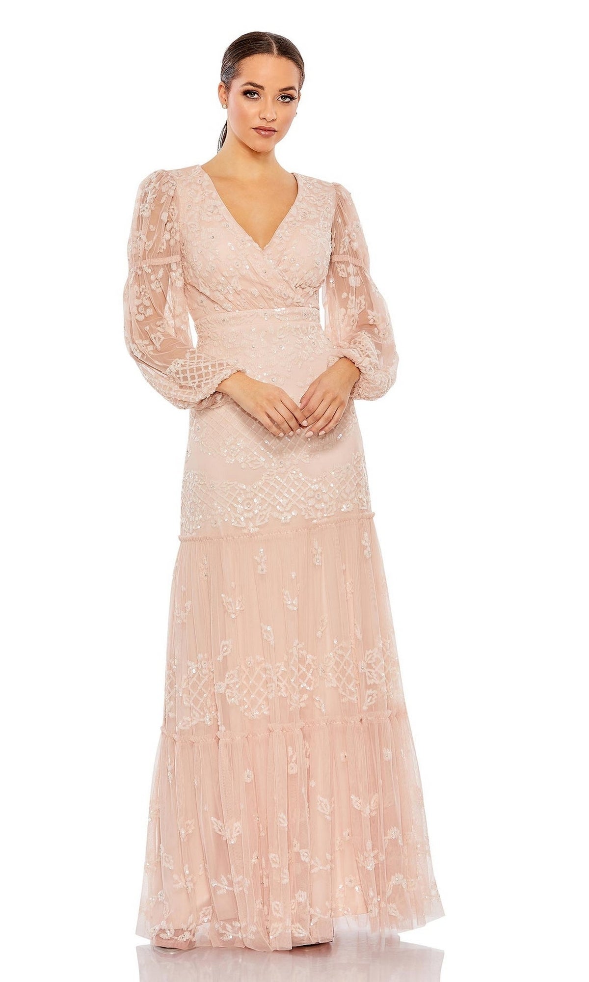 A woman models the Long Formal Dress 9197 by Mac Duggal—a blush pink, floor-length A-line dress with a v-neck, sheer long sleeves, and lace details—against a white background.